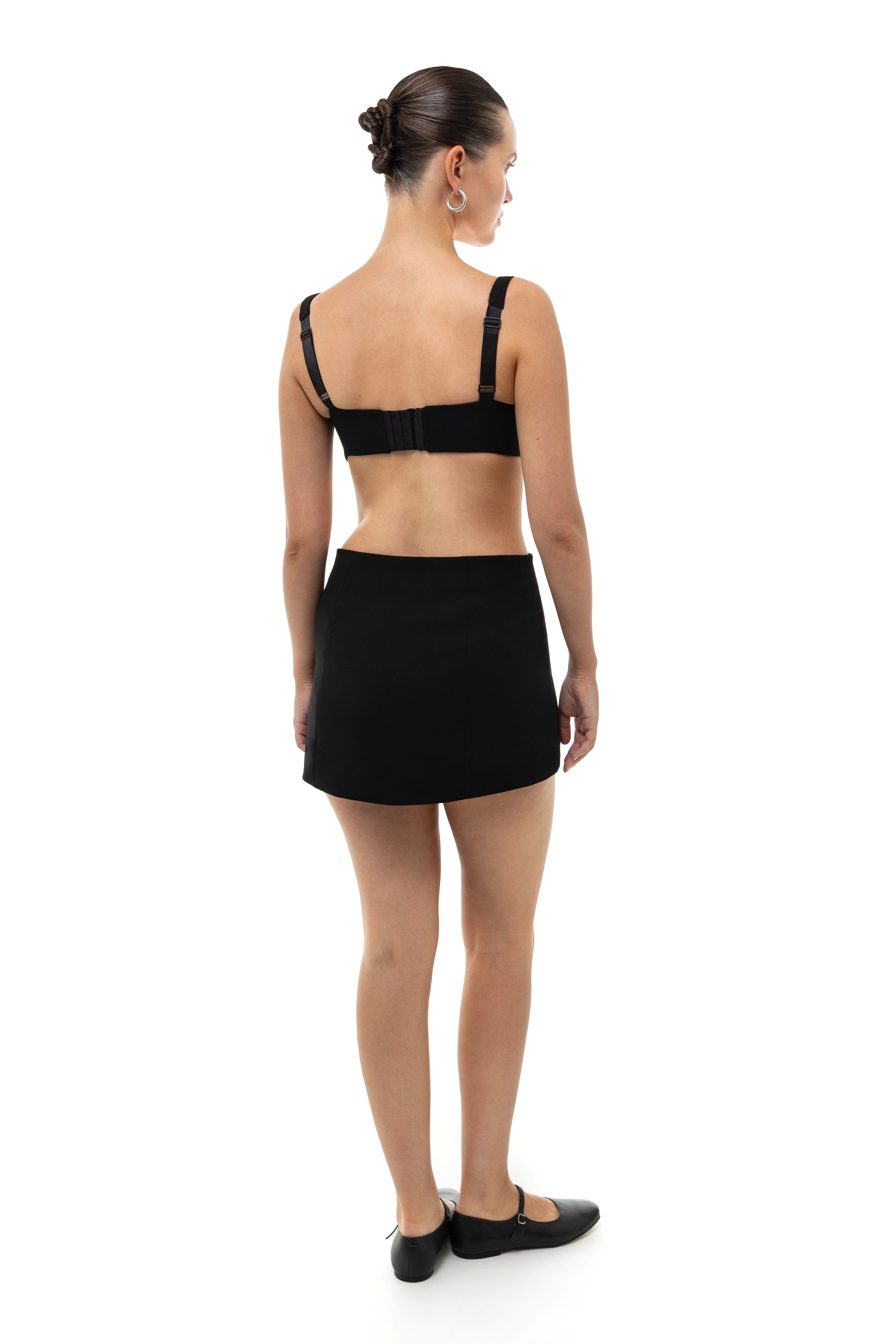 Woman wearing a black bra top, non-lingerie, and mini skirt set on a white background