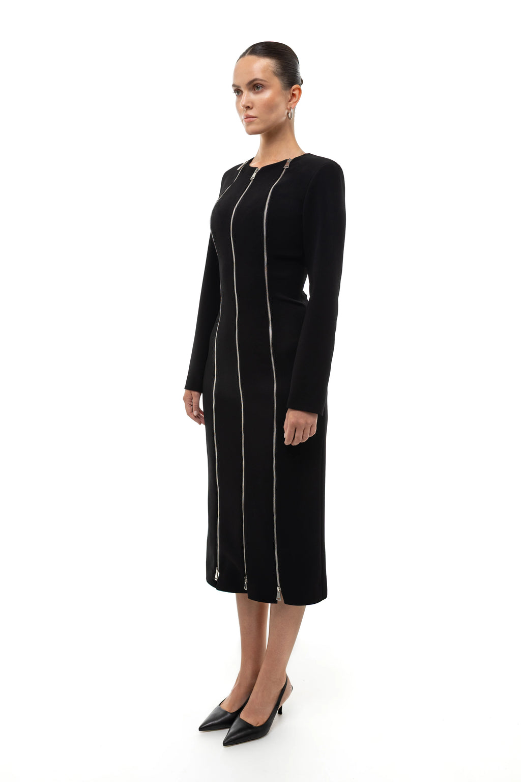Woman wearing a black midi dress with silver zippers on a white background. 