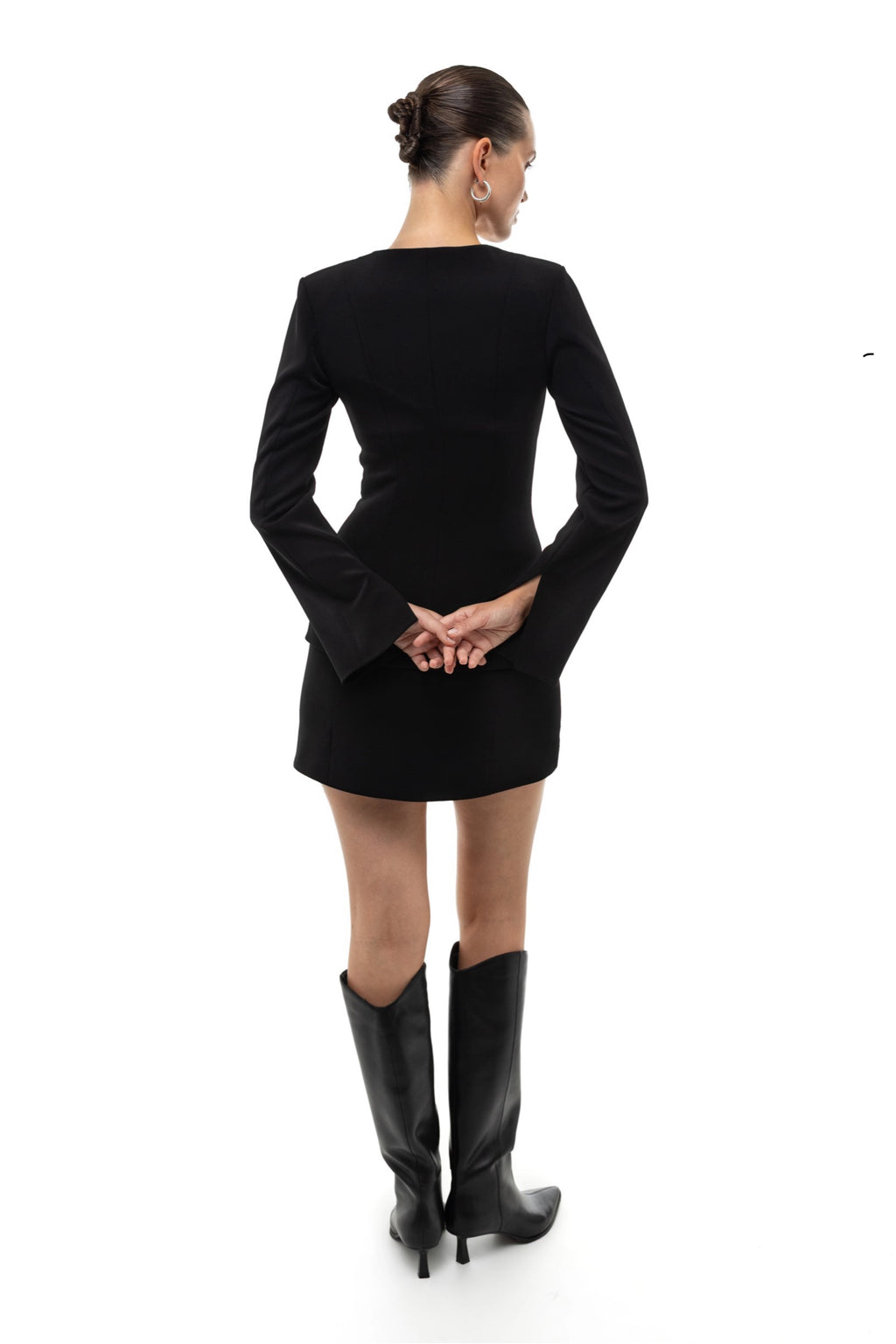 Woman wearing a black set of blazer and mini skirt and high boots on a white background. Soluje