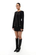 Woman wearing a black outfit with zippers on a white background. Blazer. Mini skirt. Boots. Soluje