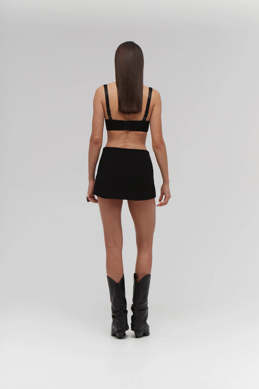 Person wearing a black outfit with high boots on a white background.