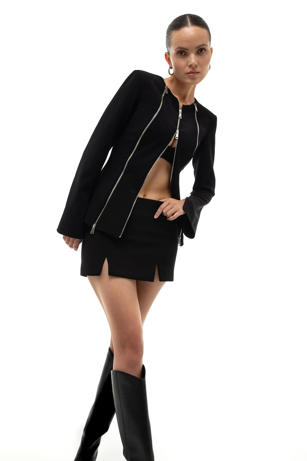 Woman wearing a black outfit with a jacket decorated with zippers and mini skirt on a white background.