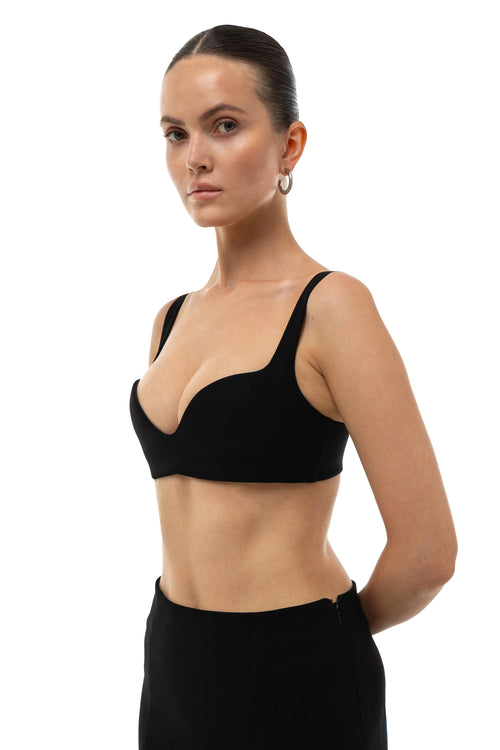 Woman wearing a non-lingerie black bra top and black mini skirt  on a white background. 