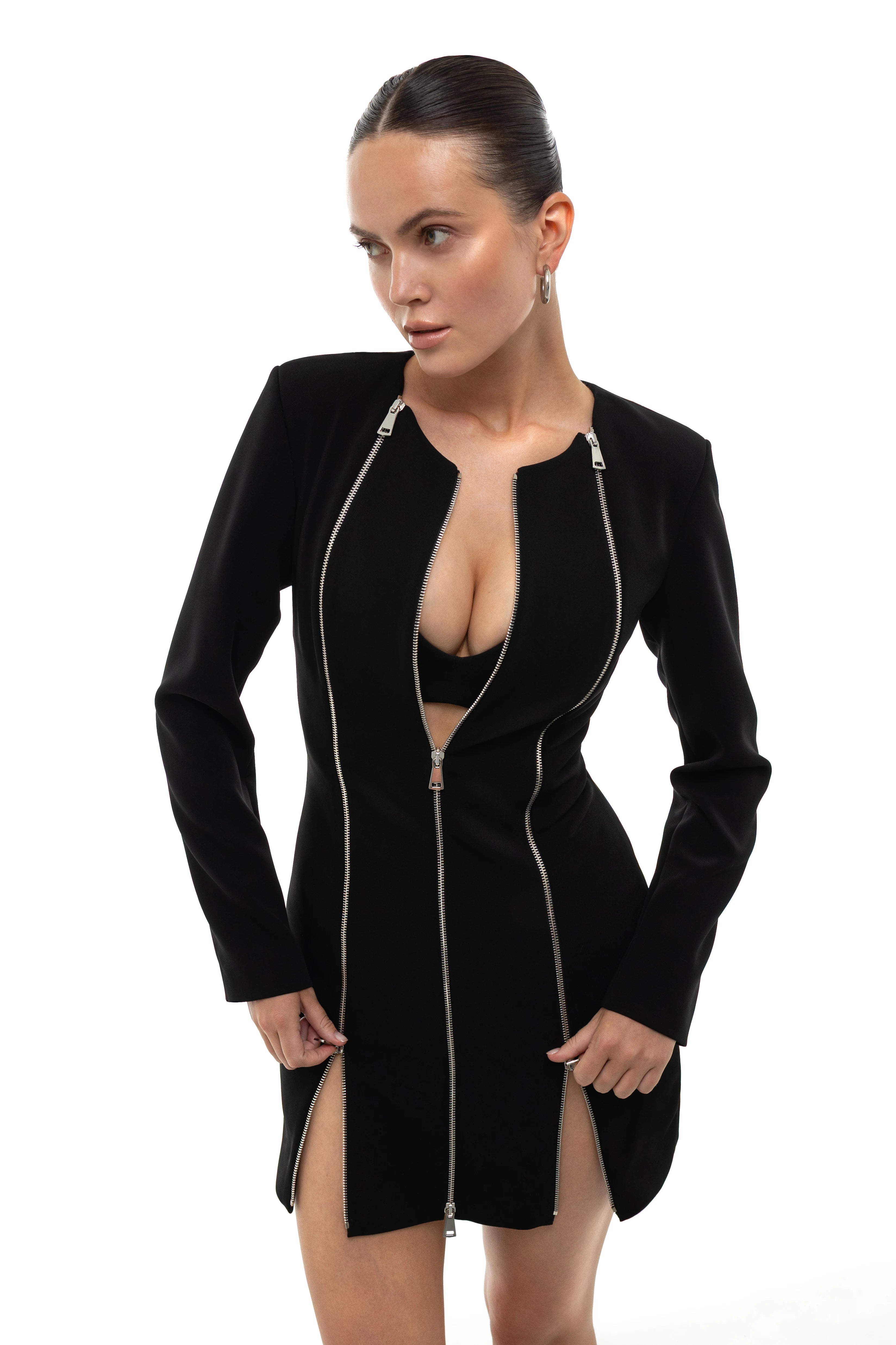 Woman wearing a black dress with a few front zippers on a white background. The central zipper is unzipped. Soluje
